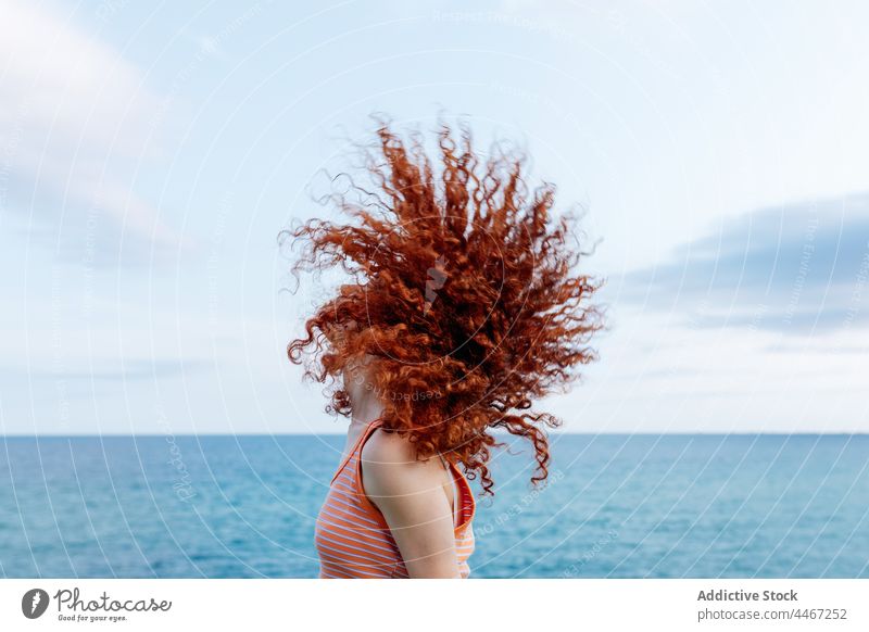 Relaxed woman whipping curly hair on seashore shaking hair chill energy carefree freedom relax motion female ginger hair red hair nature redhead water blue