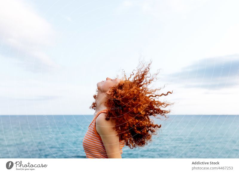 Relaxed woman whipping curly hair on seashore shaking hair chill energy carefree freedom relax motion female ginger hair red hair nature eyes closed redhead