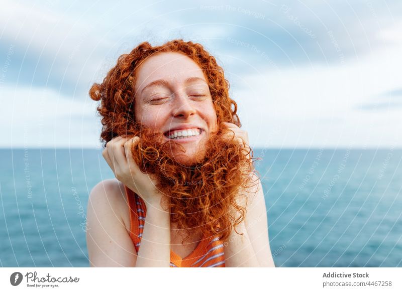 Cheerful woman touching curly hair on shore of sea funny joke personality happy expressive childish silly female redhead glee glad having fun humor portrait