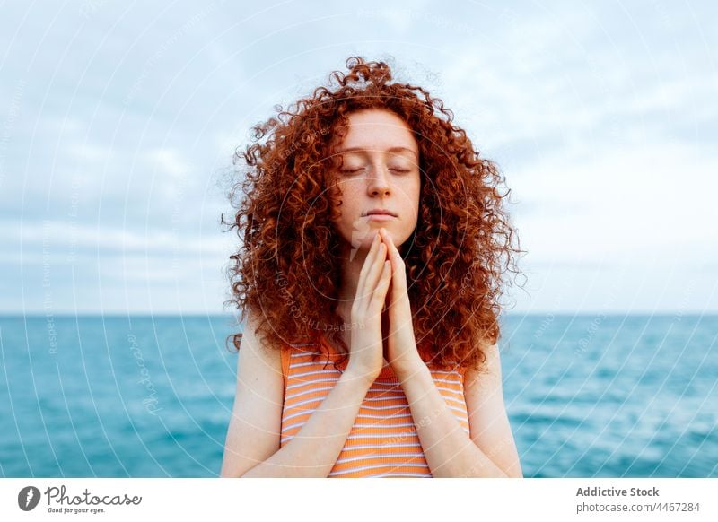 Woman with hands on chest meditating on seashore woman eyes closed beach yoga meditate gesture spirit namaste mental stress relief female harmony mindfulness