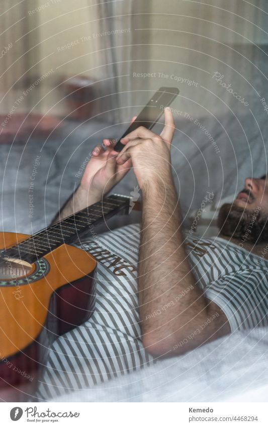 View through a window of a man with guitar lying on sofa using a phone intimacy privacy technology cell cellphone bed soft mobile comfortable musician guitarist