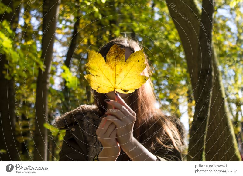 Woman with autumn leaf in front of face in forest Autumn Nature Autumn leaves Exterior shot Young woman Early fall Autumnal Autumnal colours Automn wood