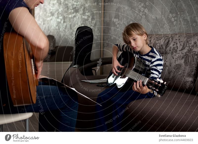 Young male musician teaches little boy student how to play the acoustic guitar and play by notes lesson instrument guitarist musical learn playing teacher