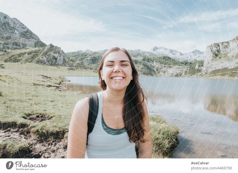 Portrait of young smiling woman with flying hair in windy day standing at mountain - carefree woman, carefree and liberty concepts, bright day journey female