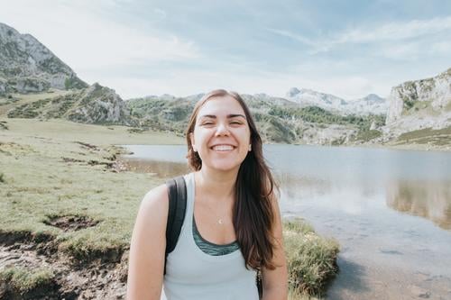 Portrait of young smiling woman with flying hair in windy day standing at mountain - carefree woman, carefree and liberty concepts, bright day journey female
