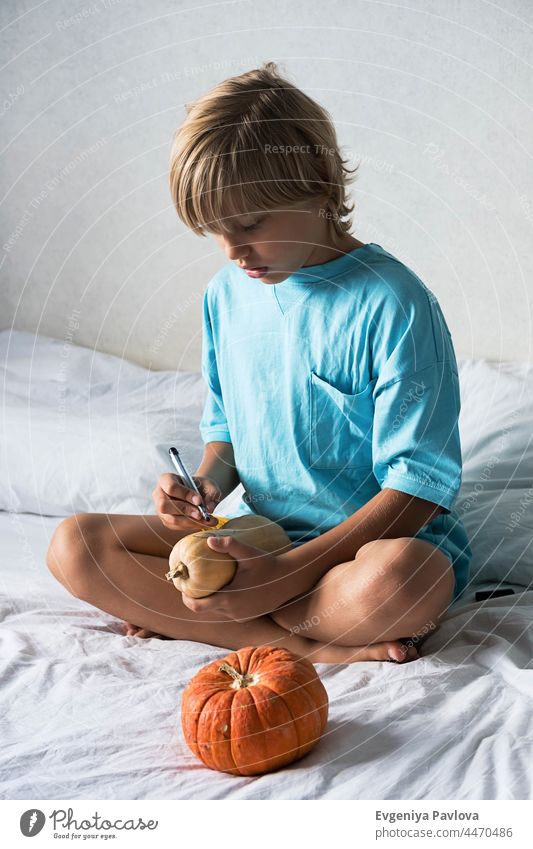Blonde boy making Jack-o-Lantern at home. Halloween DIY concept. halloween pumpkins decor diy paint felt-tip pen lifestyle fall art festive drawing kid white