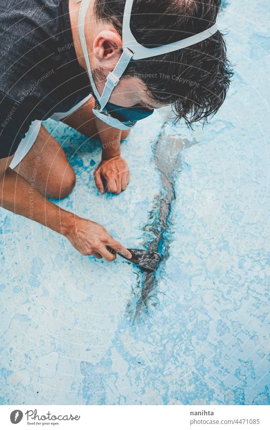 Young man working in his swimming pool maintenance diy mask putty putty knife putty palette blue turquoise job tools hard physical composition paint fix fixing