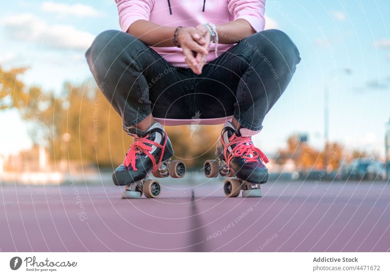 Anonymous woman wearing roller skates squatting down in park hoodie pink dreamy activity denim casual skate park smile jeans young lifestyle hobby active urban