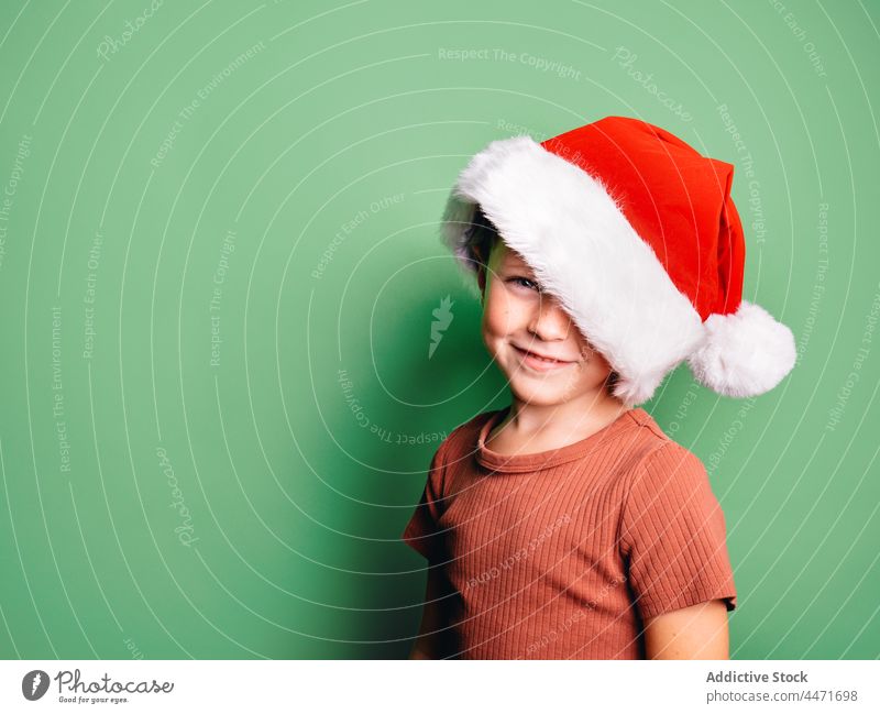 Smiling boy wearing Santa Claus hat standing in studio kid christmas santa hat event xmas holiday celebrate occasion carefree positive glad personality optimist