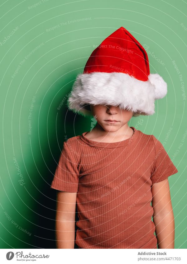 Anonymous boy in Santa Claus hat christmas holiday face covered new year upset santa claus hide event child december kid serious childhood treat unhappy winter