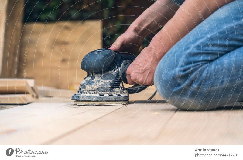 close up of a worker sanding wood planks with a grinder abrasive arm cable carpenter carpentry closeup construction craft dust electric electrical electricity