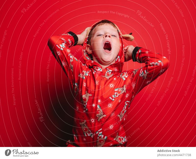 Cute child in Christmas costume yawning in red studio christmas sleepy funny new year xmas portrait boy childhood december celebrate happy pajama kid sleepwear
