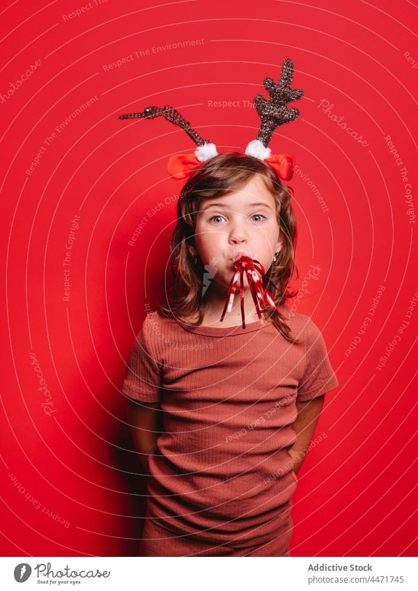 Happy child with party blower in red studio during Xmas celebration girl christmas joy celebrate holiday xmas positive portrait deer headband festive event