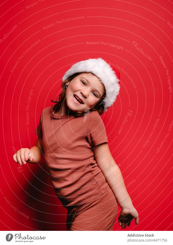 Cheerful cute kid in Santa hat smiling in red studio child santa hat christmas girl new year smile portrait model style costume glad childhood casual celebrate