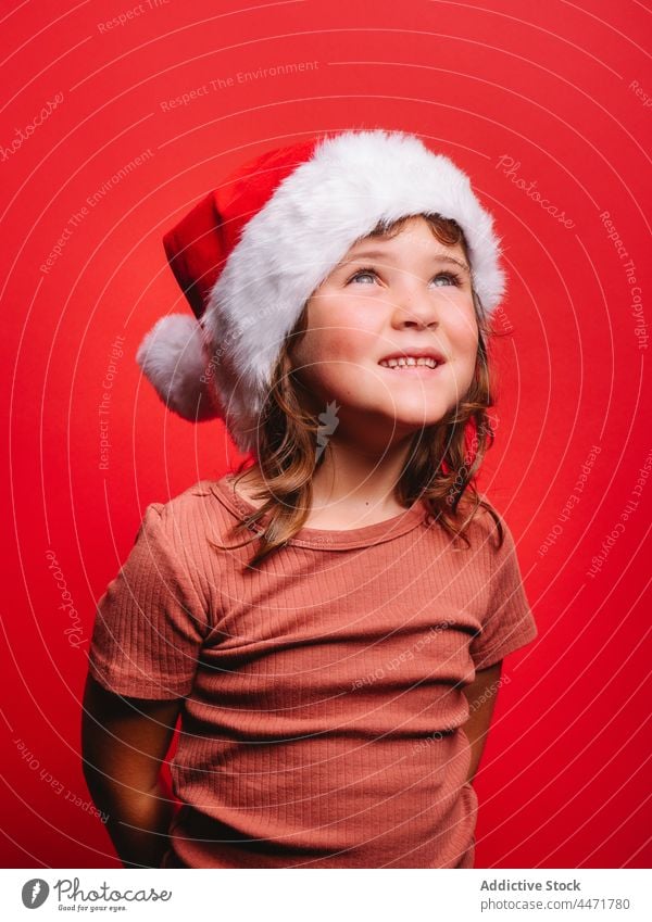 Cheerful cute kid in Santa hat smiling in red studio child santa hat christmas girl new year smile portrait model style costume glad childhood casual celebrate