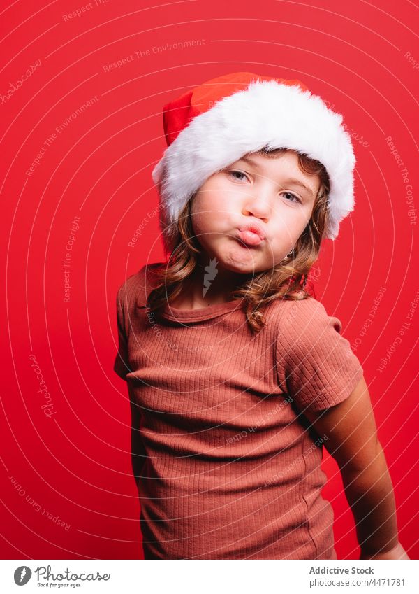 Cute kid in Santa hat pouting lips in red studio child santa hat christmas girl new year portrait model style costume make face childhood casual celebrate