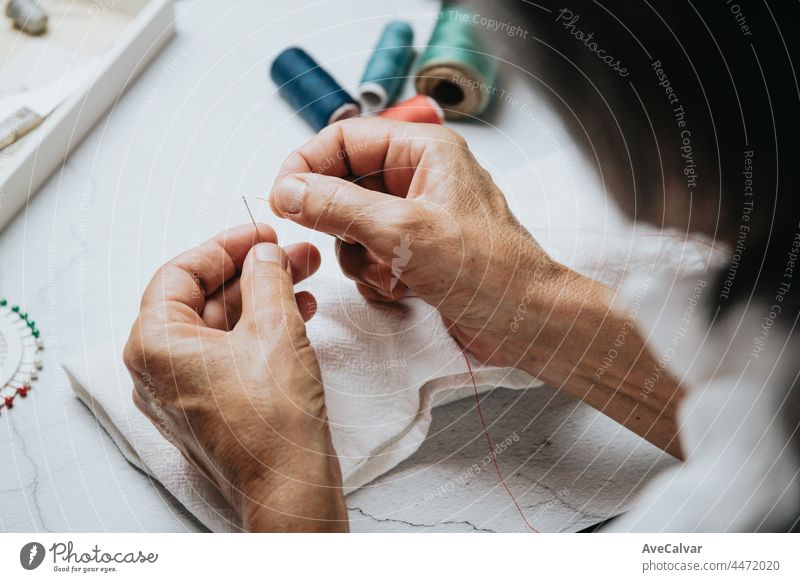Close up on woman's hands sewing needle and thread. Old woman working wasted hands .Tailor sewing some fabric. Details, low light, moody person women old woman