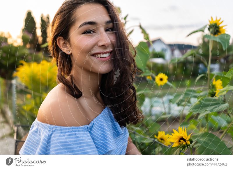 Beautiful young woman walking through an allotment pushing her turquoise bicycle with sunflowers in the basket. women Caucasian ethnicity 20-24 years Laughter