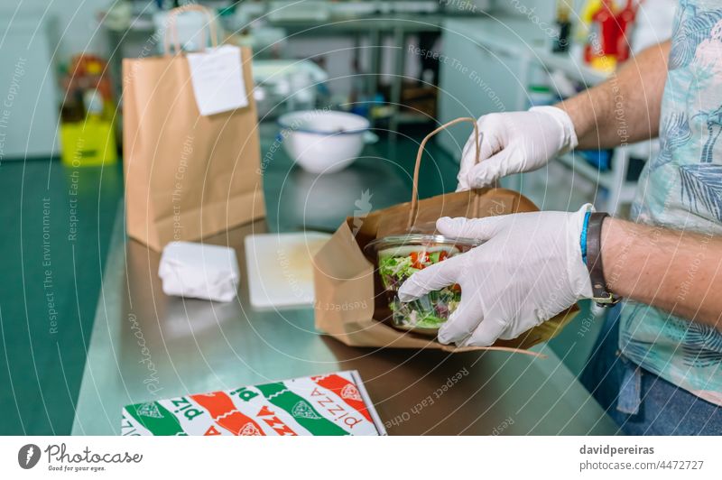 Unrecognizable cook packing a takeaway order safe food paper bag home delivery take away orders putting in salad pizza box unrecognizable professional kitchen