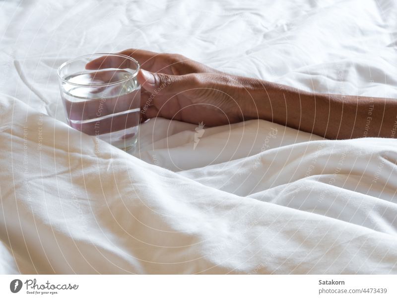 Hand holding the Glass of water on the bed crumpled blanket white glass hand soft bedroom drink hotel sheet morning messy modern home clean relaxation interior