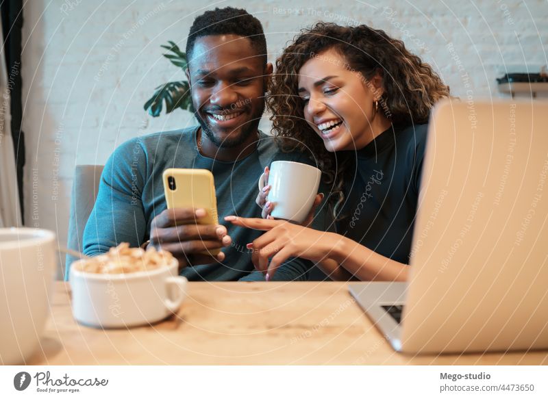 Couple using a mobile phone while having breakfast together at home. young couple indoors lifestyle quarantine food kitchen laptop technology smartphone
