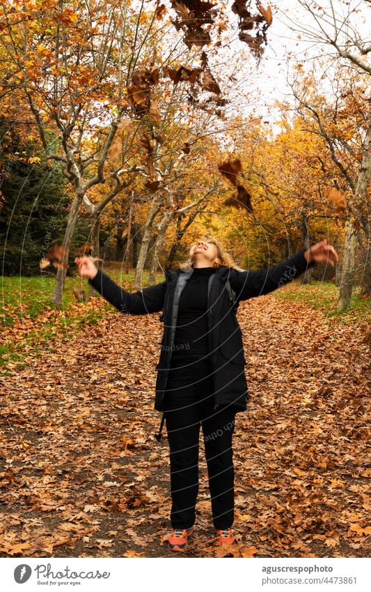 Unrecognizable woman throwing fallen leaves into the air and laughing forest autumn background ocher brown golden yellow orange colours change tree tree branch