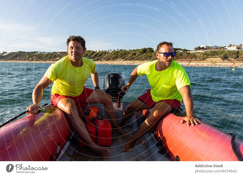 Male lifeguards riding inflatable motorboat men control sea safety sail protect float male seashore ripple water barefoot summer transport summertime occupation