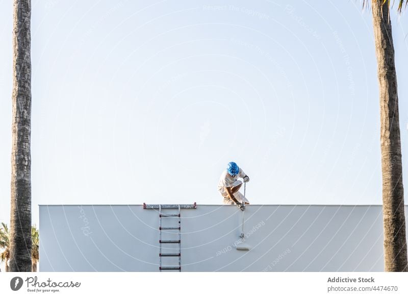 Front view of a young painter painting from the roof man helmet occupation individuality safety splattered stained sky working copy space ladder dirty