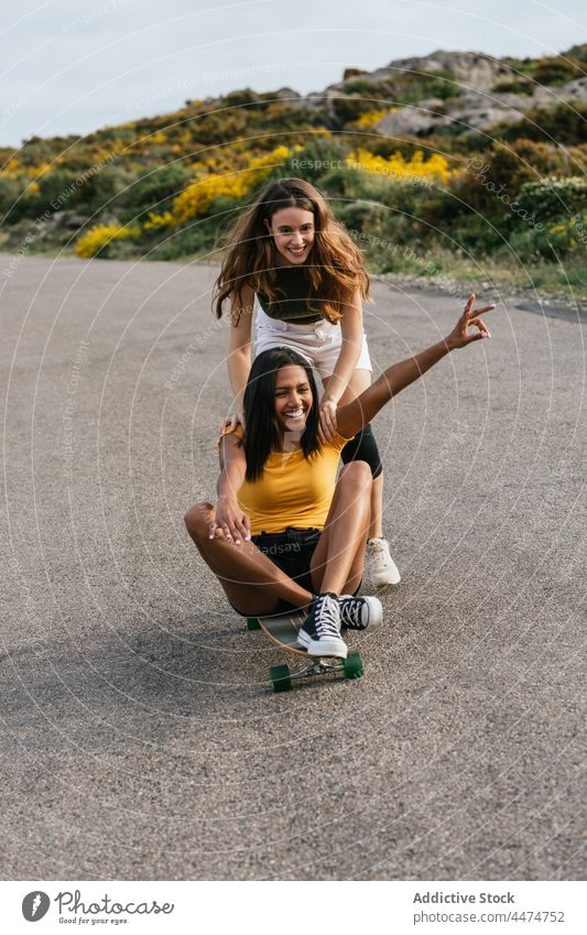 Happy diverse women riding longboard on road friend ride v sign hobby gesture happy friendship leisure female best friend cheerful together two fingers victory