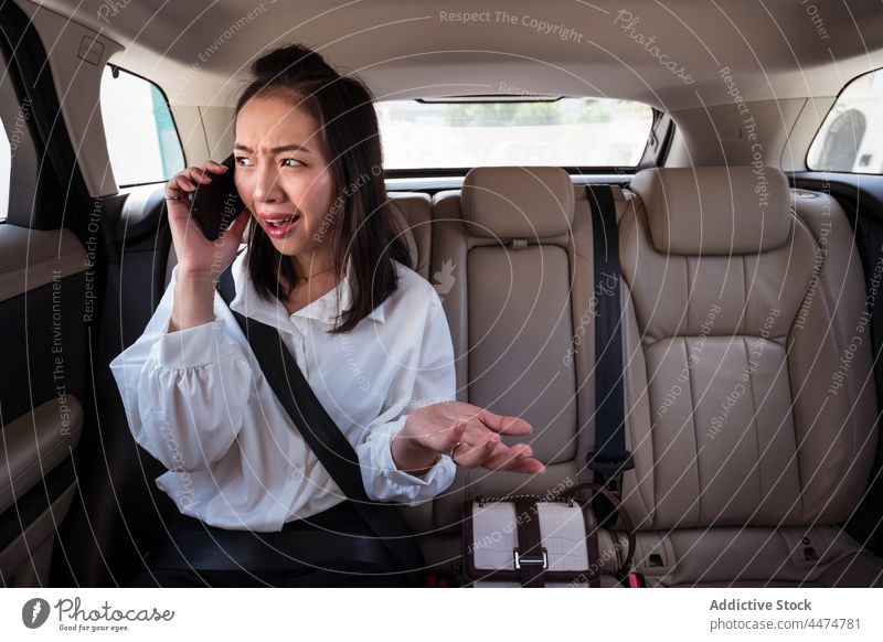 Dazed Asian woman having phone call on backseat in car passenger taxi daze smartphone using unbelievable reaction confuse female disbelief doubt expressive
