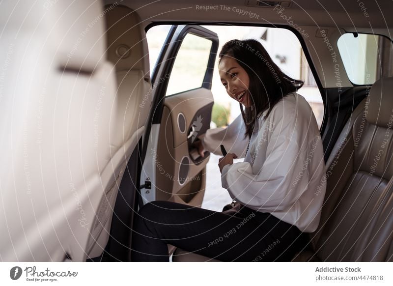Smiling Asian woman getting into taxi passenger enter backseat positive cab formal car door open female departure service public ride cellphone automobile enjoy