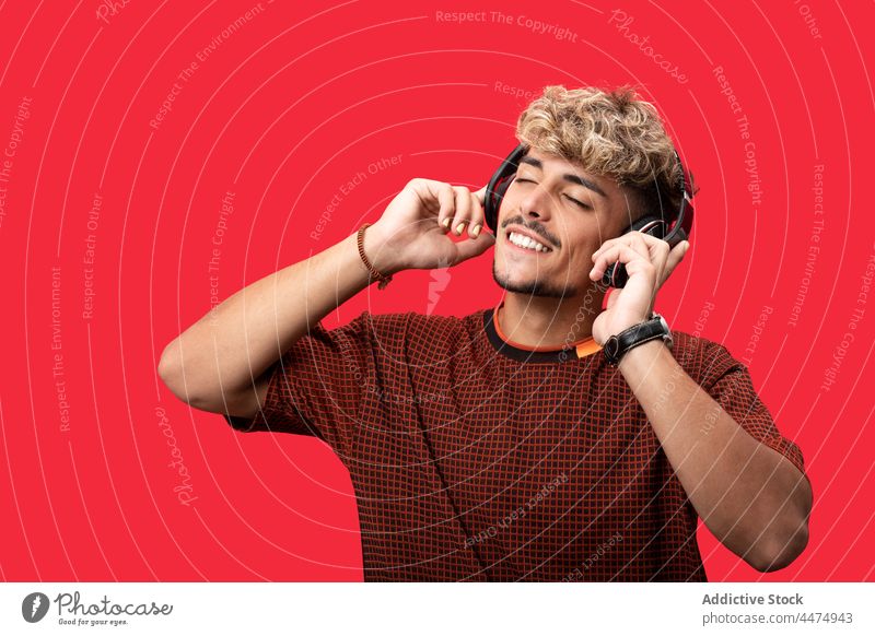 Smiling curly haired man listening to music in headphones song using playlist enjoy wireless style male optimist carefree hobby meloman melody positive glad
