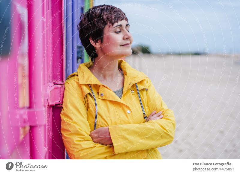 side view of relaxed woman with eyes closed wearing yellow raincoat over pink and purple background. Colorful Outdoors lifestyle portrait colorful outdoors city