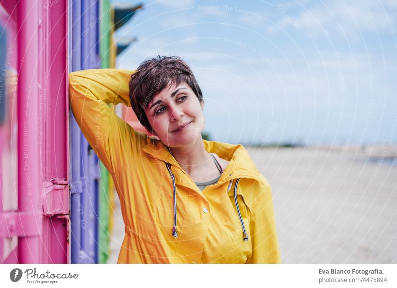 side view of relaxed woman wearing yellow raincoat over pink and purple background. Colorful Outdoors lifestyle portrait colorful outdoors city urban beautiful