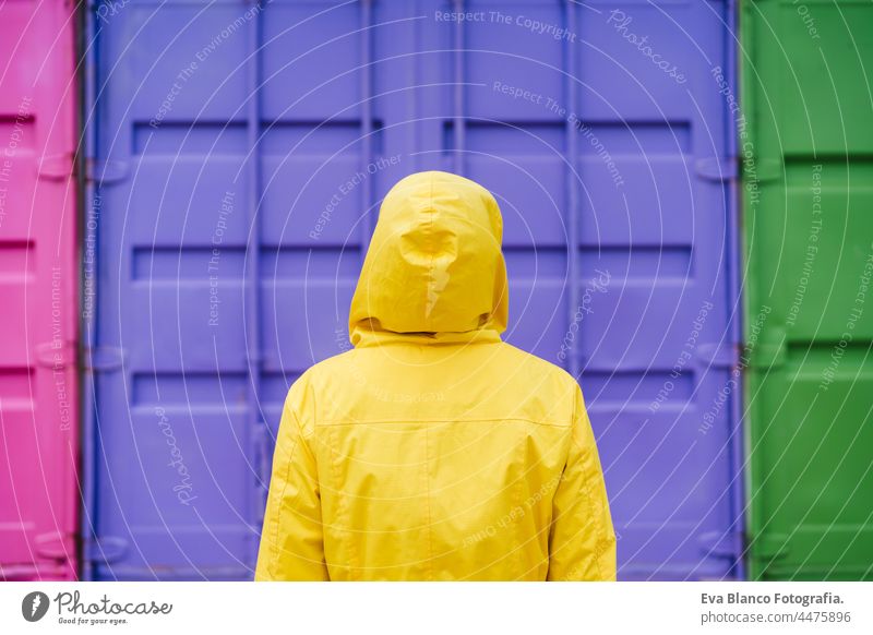 back view of woman with hood wearing yellow raincoat over pink and purple background. Colorful Outdoors lifestyle portrait colorful outdoors city urban relaxed