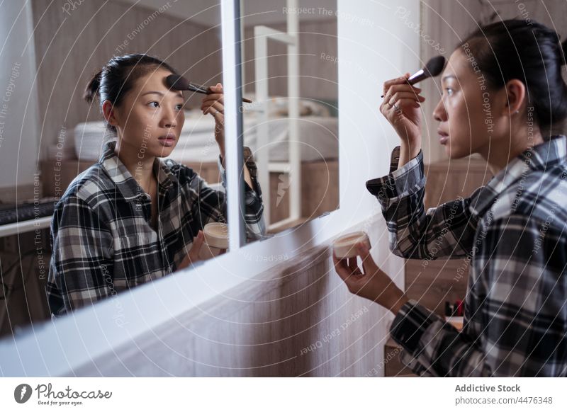 Young woman applying makeup against mirror bedroom powder appearance reflection routine light home female asian woman ethnic young cosmetic attractive apartment