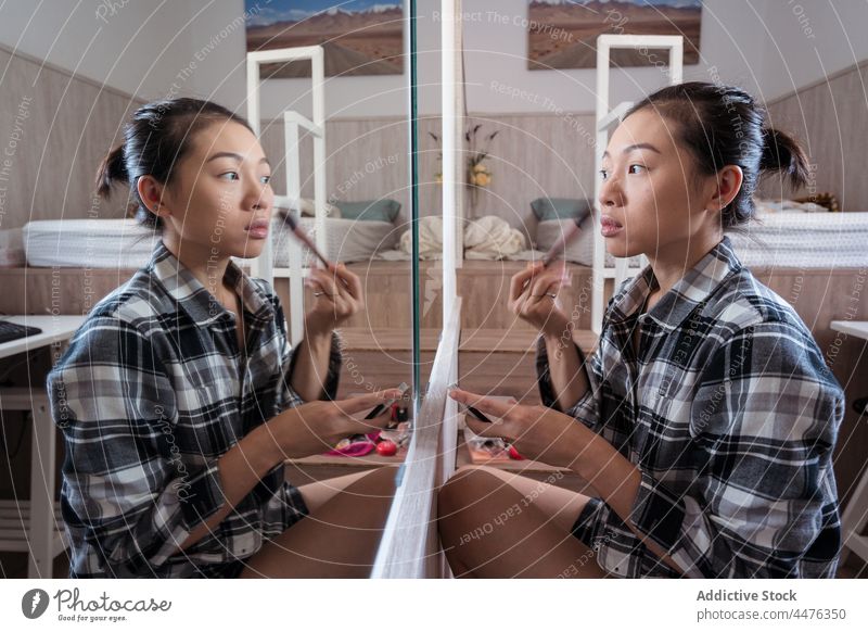 Young woman applying makeup against mirror bedroom powder appearance reflection routine light home female asian woman ethnic young cosmetic attractive apartment