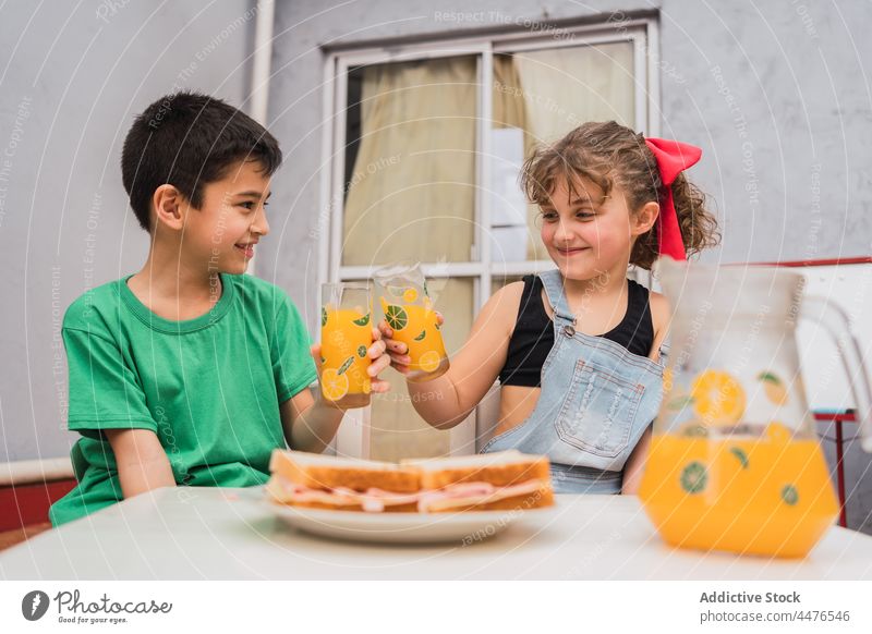 Happy kids clinking with juice near sandwiches children drink beverage food childhood snack appetite hungry light room adorable cute girl sibling tasty yummy