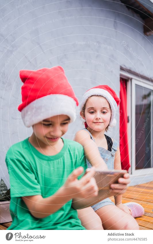 Children with smartphone with santa hats children kid christmas childhood holiday browsing hobby surfing cellphone headwear festive colorful light wooden