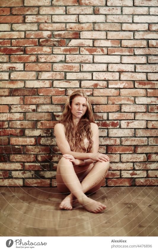 Full body image of a naked young woman with freckles and red hair sitting on the floor in front of a brick wall portrait Near proximity Emanation tranquillity