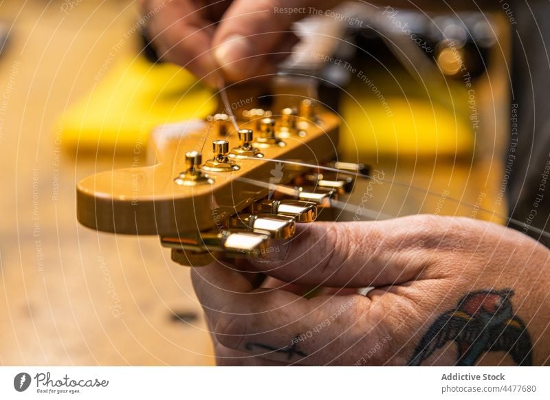Professional craftsman installing strings on guitar musician instrument guitarist workshop equipment male tattoo skill professional hobby worker fix repair
