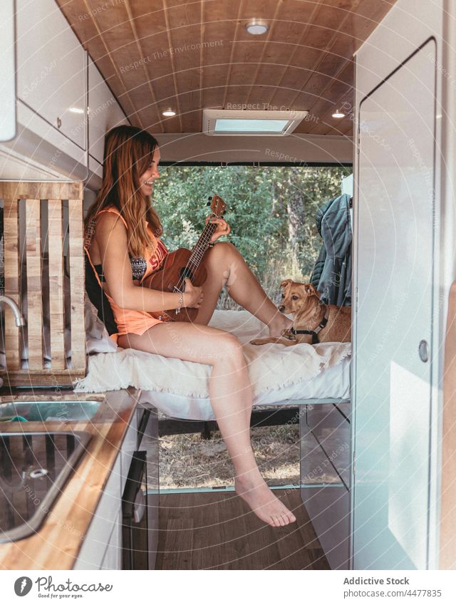 Traveler playing ukulele in camper woman traveler van dog trip together female spain parked cheerful acoustic music instrument pet owner animal bed happy smile