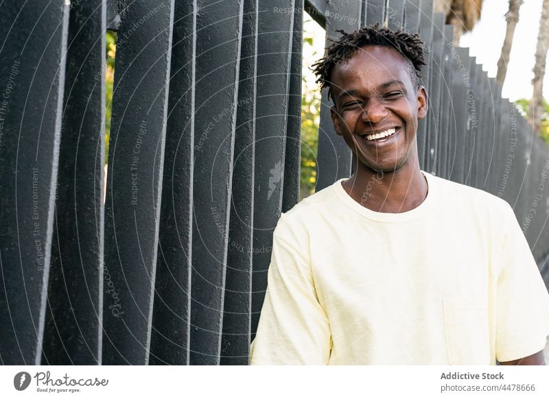 Happy African American man standing at fence cheerful casual smile short hair portrait urban happy joy optimist toothy smile hairstyle glad carefree