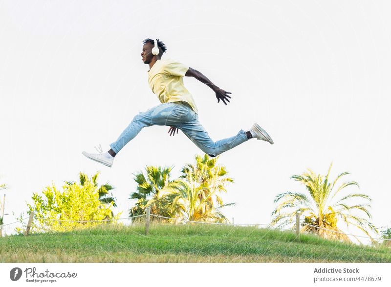Energetic black man jumping with split in park freedom activity energy casual active outfit leap lifestyle trick motion summer jeans african american arm raised