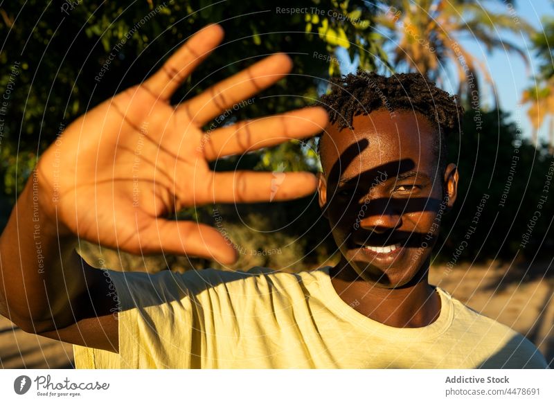 Black man with toothy smile looking at camera cover face positive friendly sunset cheerful gesture sunlight human face portrait glad african american pleasant