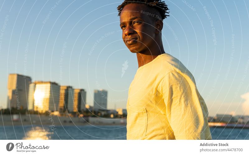 Black man looking away on street sky sunset sundown calm ocean building evening peaceful outfit city sea male african american black ethnic style appearance