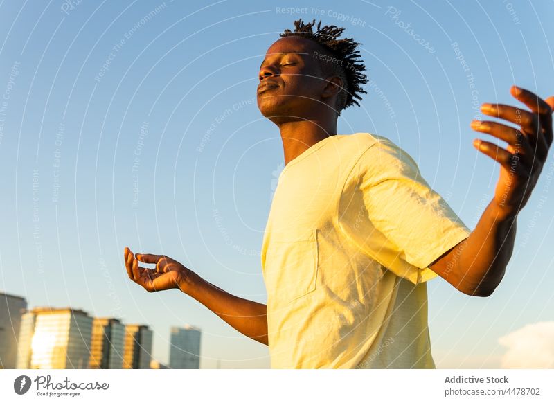 Black man with raised arms on street sky sunset sundown calm building evening peaceful outfit city male african american black ethnic style appearance summer