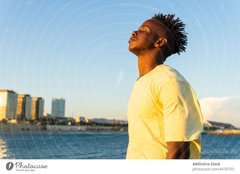Black man with eyes closed on street sky sunset sundown calm building evening peaceful outfit city male african american black ethnic style appearance summer