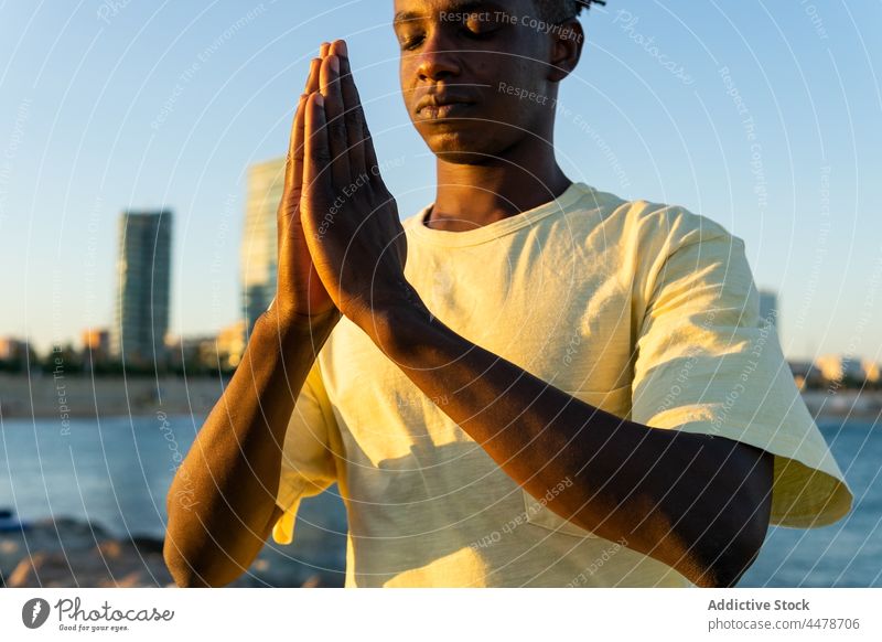 Black man with eyes closed on street sky namaste sunset sundown gesture hands calm building evening peaceful outfit city male african american black ethnic