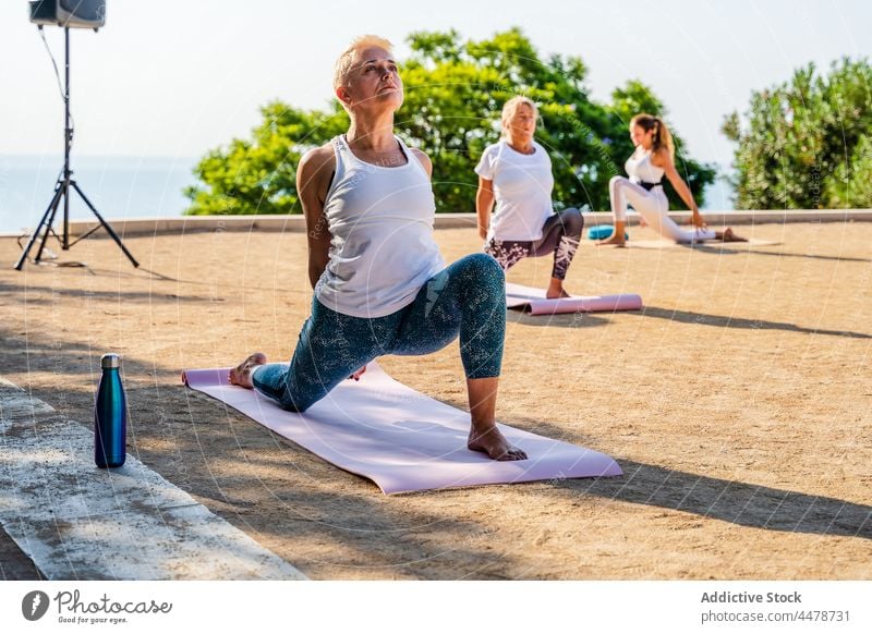 Women doing crescent lunge on knee with hands interlaced during yoga  session - a Royalty Free Stock Photo from Photocase